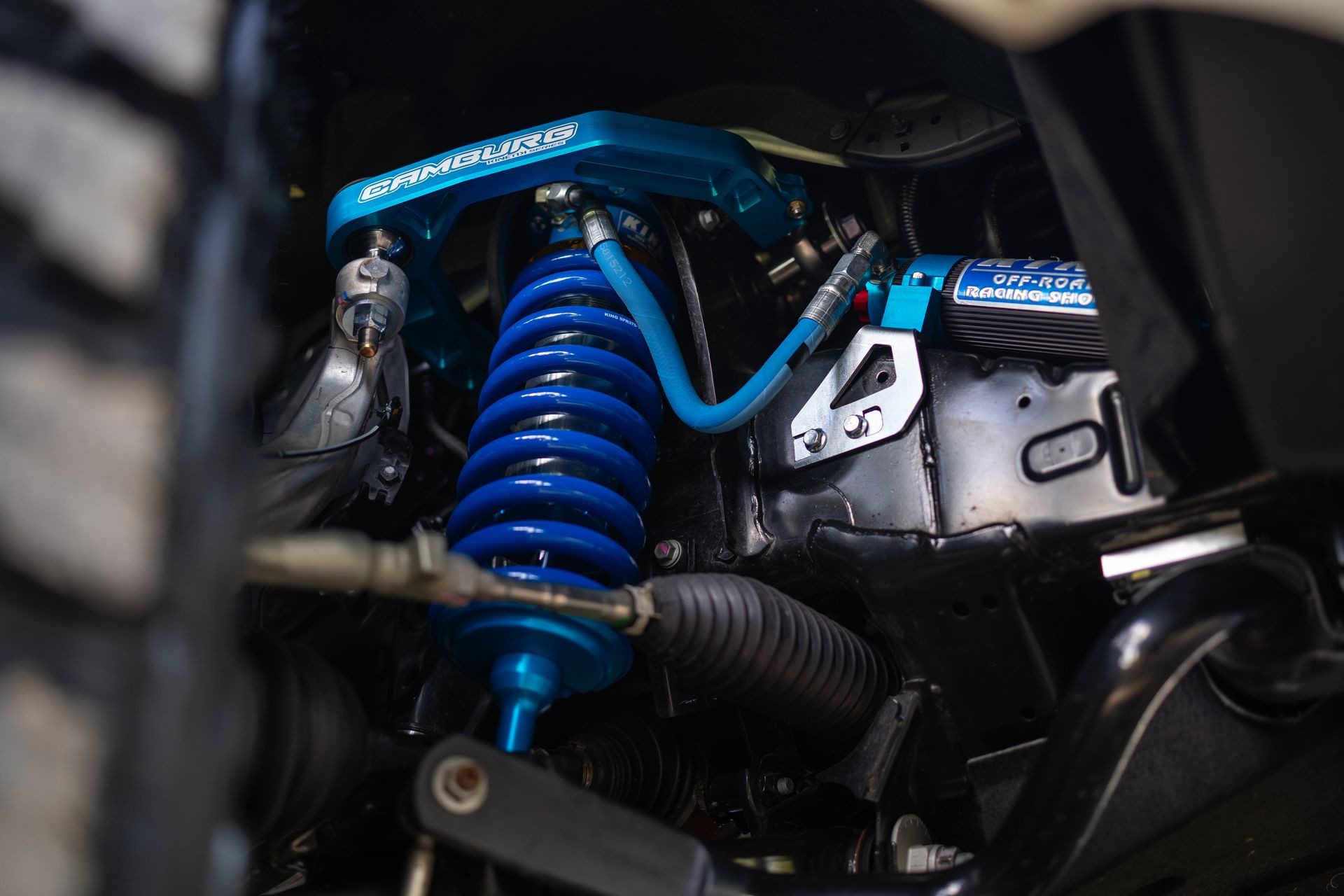 Close-up of off-road racing shock absorber system with blue coil spring and hydraulic components.